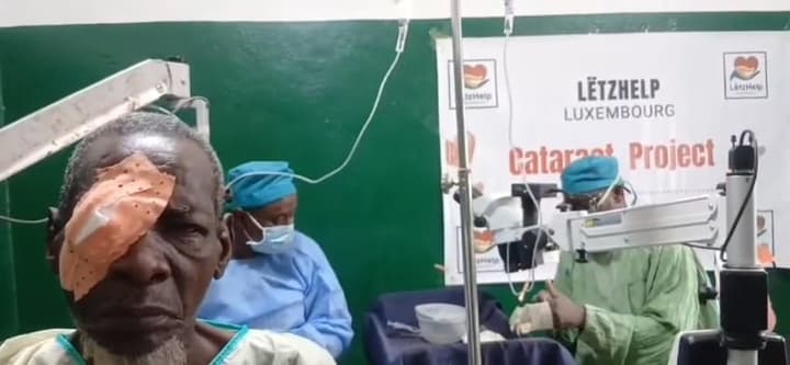 A patient with a freshly bandaged eye, while the surgeons move on to the next operation behind him