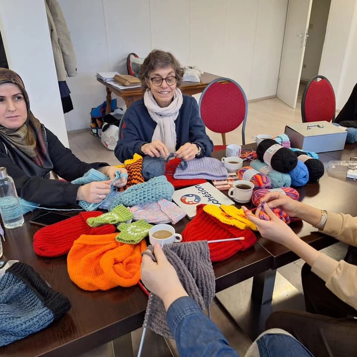 Volunteers knitting and crocheting hats around a table full of wool