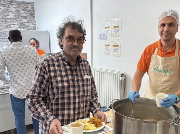 Serving the aşure: a guest with his tray and our volunteer filling cups